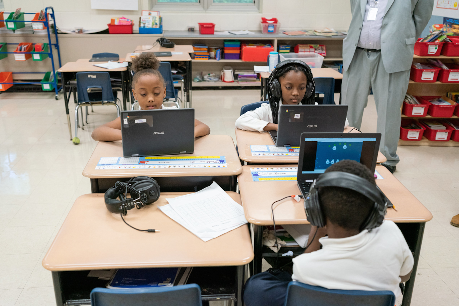 Elementary students engaged in computer-based testing using laptops and headphones in a classroom setting